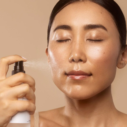 Person applying a mist spray to their face with a neutral background