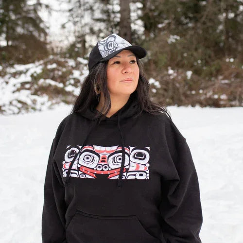 Person wearing a black hoodie with a colorful design and a cap in a snowy outdoor setting
