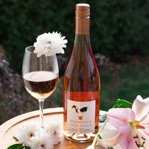Bottle of Magnotta RosΓ© wine with a glass of wine and flowers on a wooden surface.