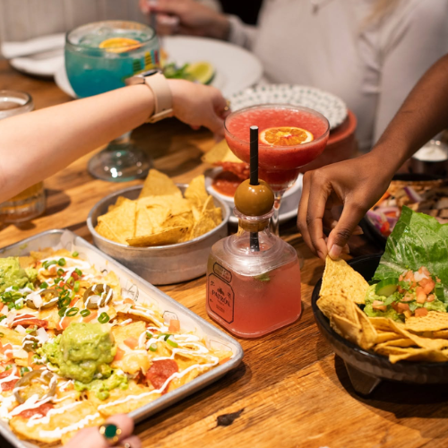 People enjoying nachos, drinks, and snacks at a table at 3 amigos.