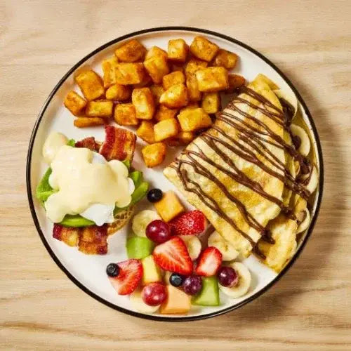 Breakfast plate with banana crepes, fresh fruit, eggs Benedict, and crispy potatoes