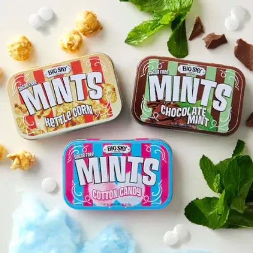 Three tins of Big Sky Mints with candy and mint leaves on a white background