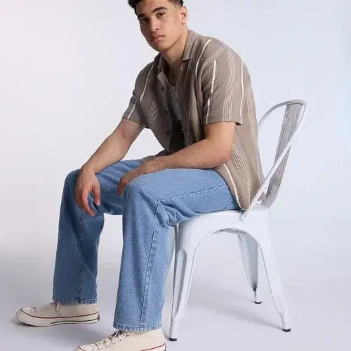 Person sitting on a white chair wearing a striped shirt and jeans.