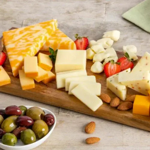 Assorted cheeses, fruits, and nuts on a wooden board with a bowl of olives.