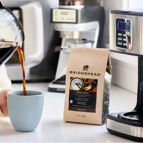 Person pouring coffee into a cup with a bag of Bridgehead coffee and coffee maker in the background.