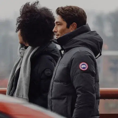 Two people wearing dark jackets with a visible brand logo, standing outdoors.