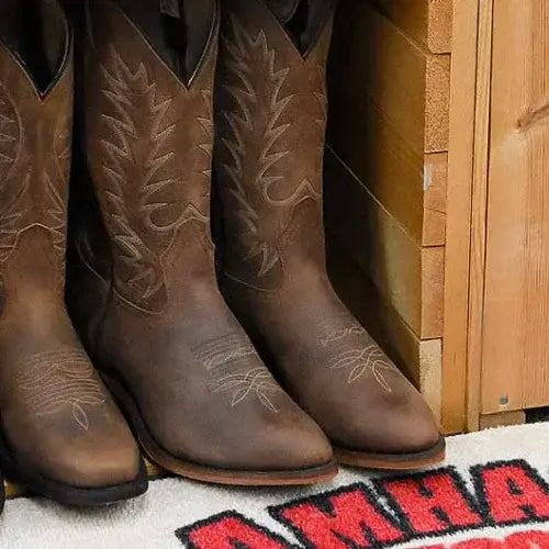 Three brown cowboy boots with floral patterns on a wooden floor.