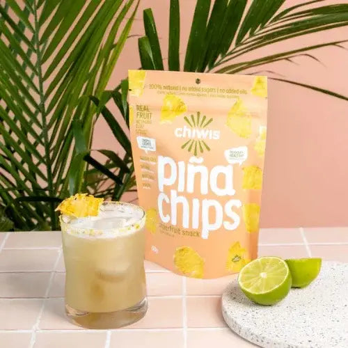 Packaging of chiwis piña chips with a cocktail and lime on a tiled surface.