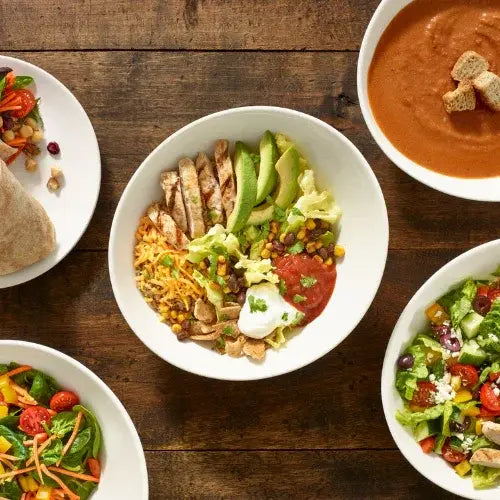 Assorted dishes including burritos, salads, and a bowl of soup on a wooden table.