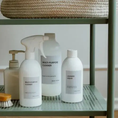 Set of cleaning products including a spray bottle and bottles labeled 'Multi-Purpose Cleaner' and 'Laundry Liquid' on a green metal shelf.