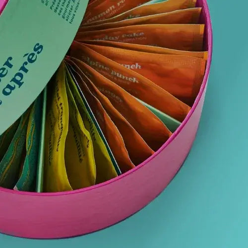Colourful tea packets in a pink container on a teal background