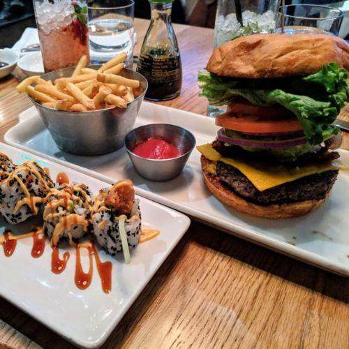 Gourmet cheeseburger with lettuce, tomato, and onion served with fries, ketchup, and sushi rolls at Earls restaurant