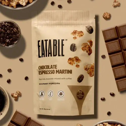 Eatable Chocolate Espresso Martini popcorn package surrounded by coffee beans, chocolate bars, and popcorn.