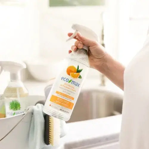 Person holding an eco-max cleaning spray bottle in a kitchen setting