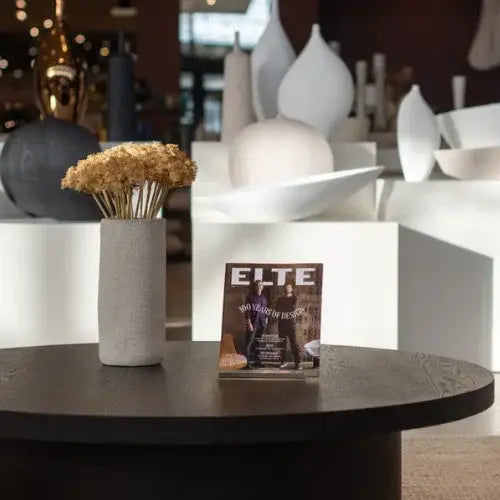 Table with a magazine titled 'ELTE', vase with dried flowers, and decorative bowl.