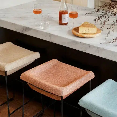 Three cushioned stools in front of a marble countertop with drinks and cheese.
