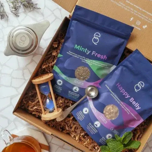 Two blue packages labeled 'Minty Fresh' and 'Happy Belly' in a cardboard box with a sand timer and spoon.