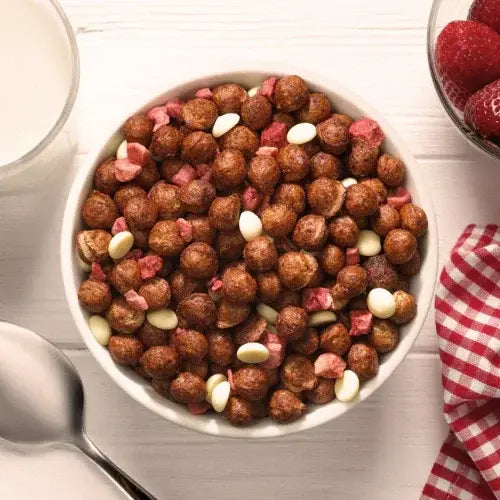 Bowl of chocolate cereal with toppings on a wooden table.