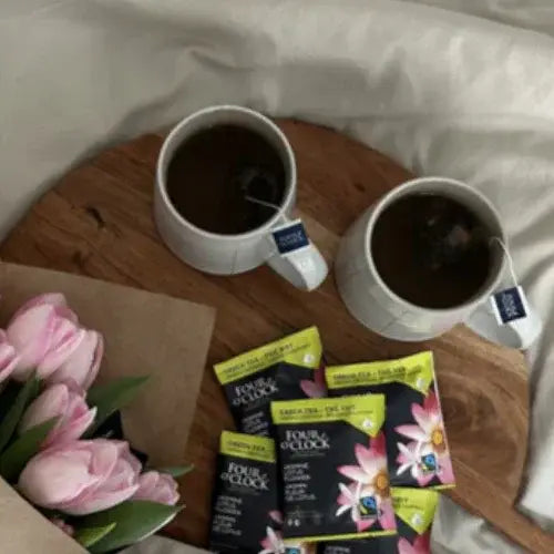 Two cups of tea on a wooden tray with Four O'Clock Tea packages and pink tulips.