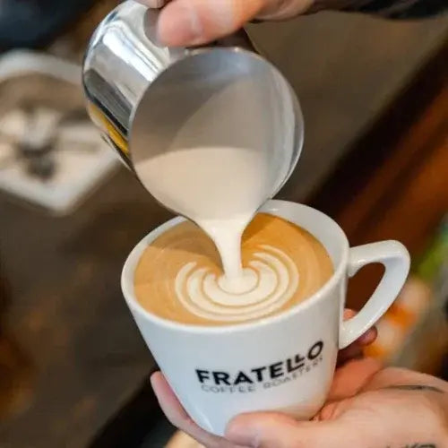 Person pouring milk into a Fratello coffee cup with latte art.