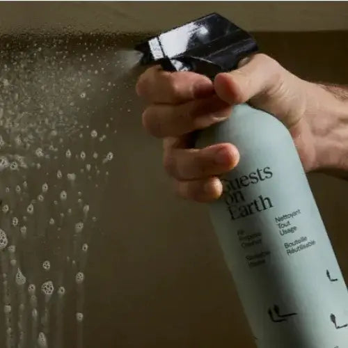 Person holding a spray bottle labelled 'Guests on Earth' over a shower head with water spraying.