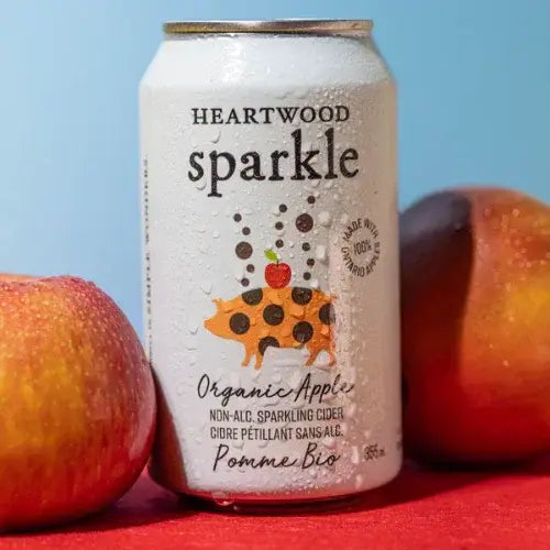 Can of Heartwood Sparkle Organic Apple cider with apples on a red surface and blue background