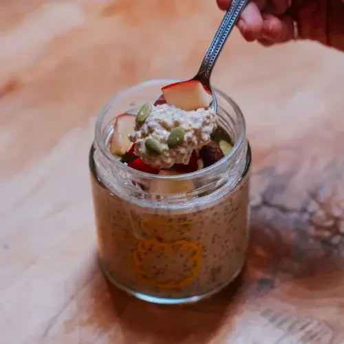 Glass jar with chia pudding, apples, and seeds on a wooden surface