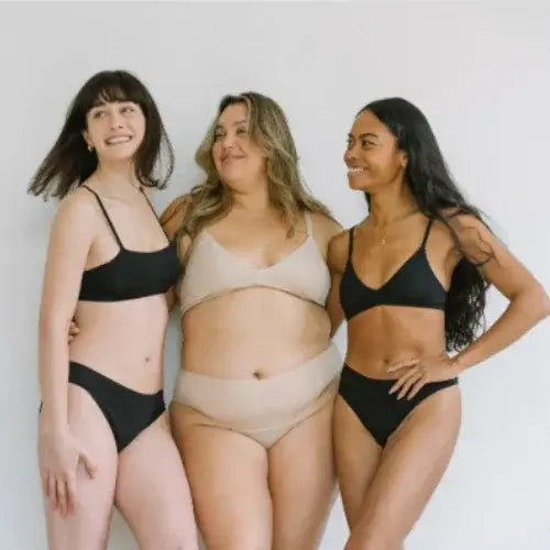Three women posing together in swimwear against a plain background
