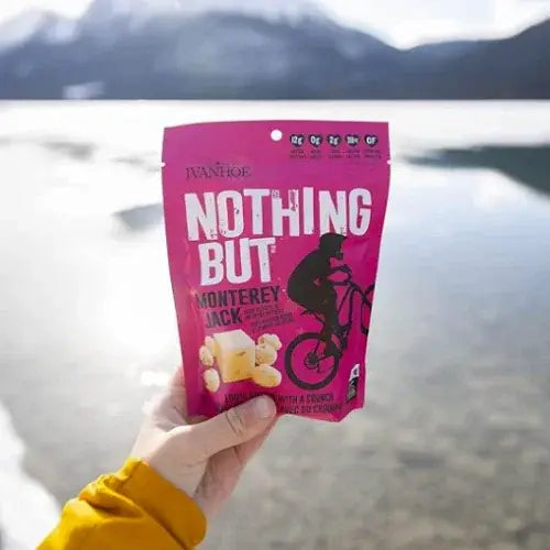 Person holding a 'Nothing But' Monterey Jack cheese snack packet with a mountainous landscape in the background.