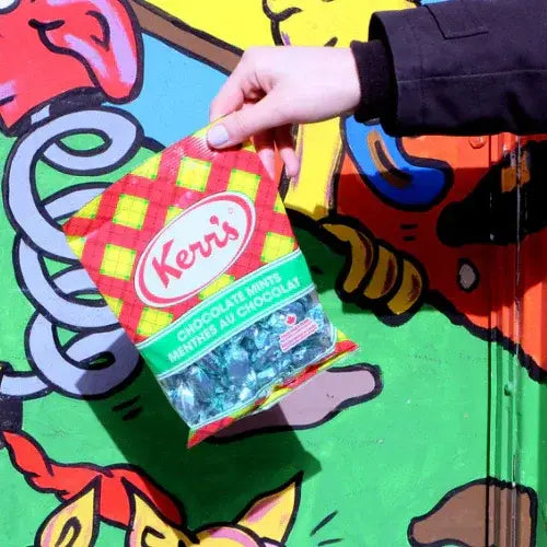 Hand holding a Kerr's chocolate minis package against a colorful, abstract background