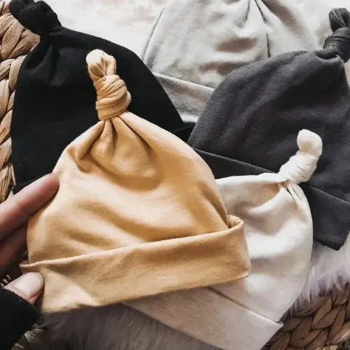 Three tied fabric bags in black, beige, and gray on a woven surface.