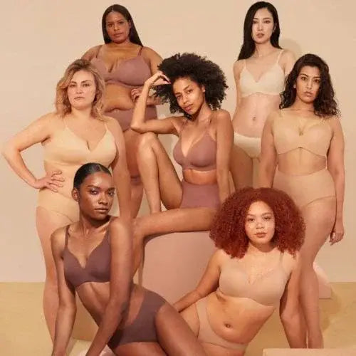 Diverse group of women wearing nude-toned Knix bras and underwear, standing and sitting confidently against a beige background, showcasing body positivity and inclusivity.