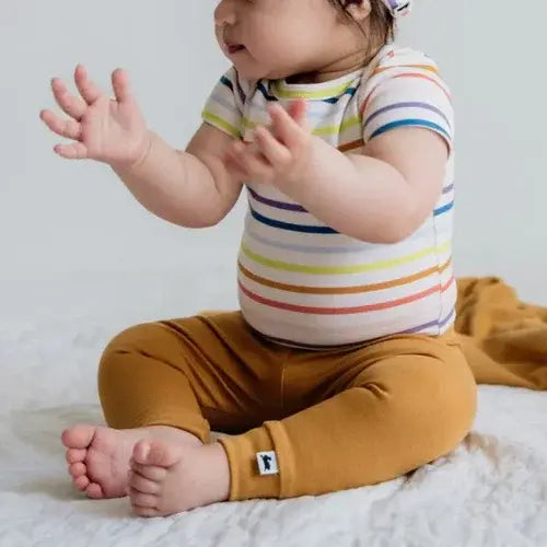 Baby wearing a colourful striped Little & Lively shirt and mustard pants on a white background