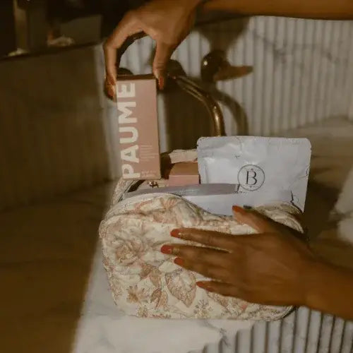 Person reaching into a floral-patterned bag with various items including a box labeled 'PAUME'.