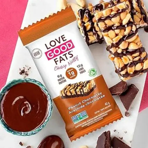 Chocolate bar with peanut toppings and packaging on a pink background.