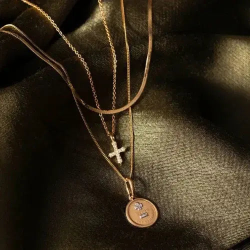 Layered gold necklaces with cross and medallion pendants on satin fabric – Curated fine jewellery from Canadian-owned Magpie Jewellery