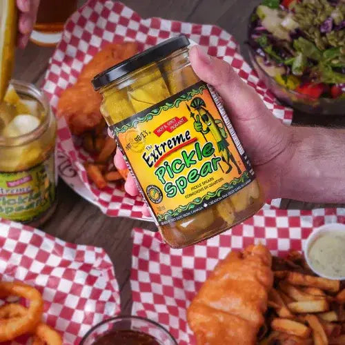 Person holding a jar of Extreme Pickle Spear with a casual dining setting in the background.