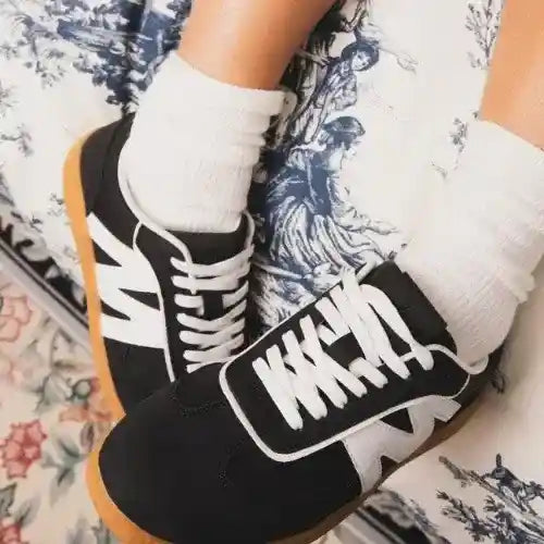 Black and white sneakers with brown soles worn by a person on a floral-patterned surface.