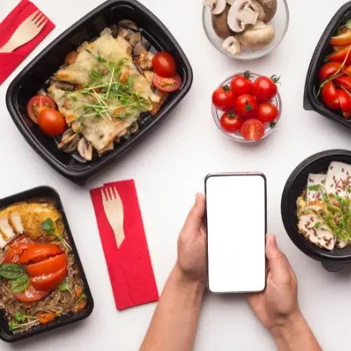 Hands holding smartphone next to healthy prepared meals in takeout containers – Fresh meal delivery service with app ordering