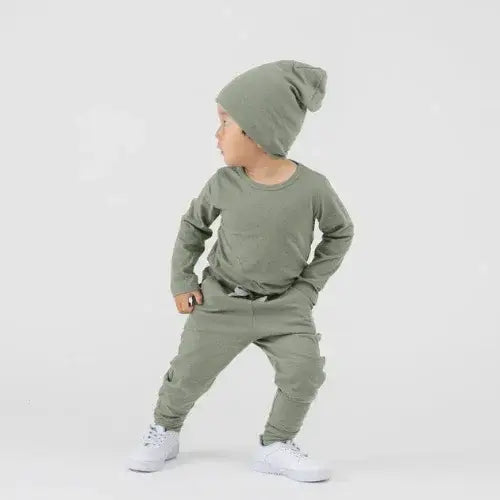 Child wearing a green mini mioche outfit with a beanie on a white background