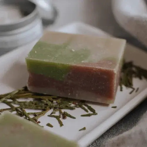 Three-layered soap with green, pink, and white on a white plate with dried herbs