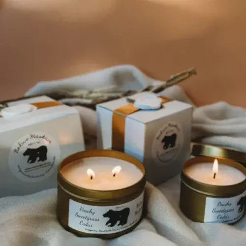 Two lit candles in gold tins with labels on a soft fabric background
