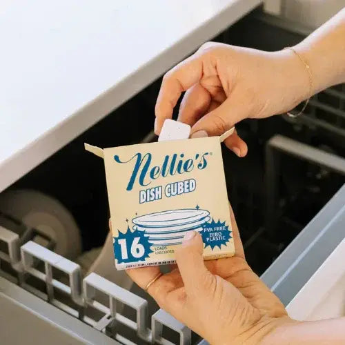 Person holding a box of Nellie's Dish Cubed in front of an open dishwasher.
