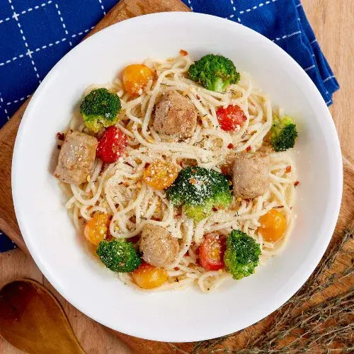 Bowl of pasta with chicken pieces and vegetables on a wooden surface.