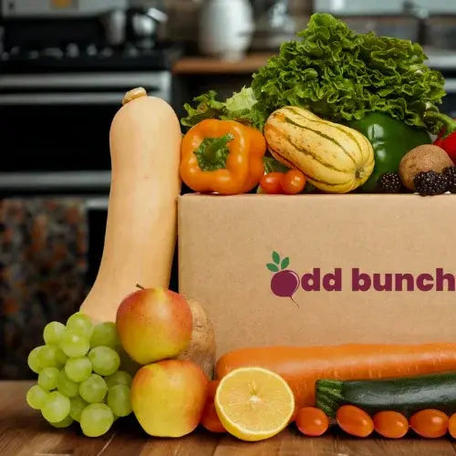 Box of assorted fruits and vegetables with 'odd bunch' branding on a kitchen counter.