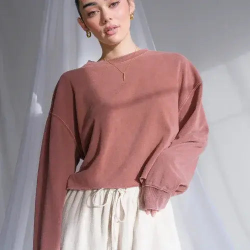 Person wearing a pink sweatshirt and white pants against a plain background