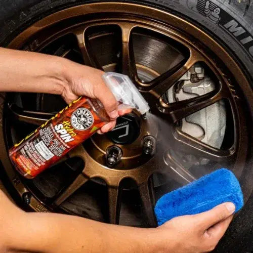 Person cleaning a car wheel with a spray bottle and blue sponge