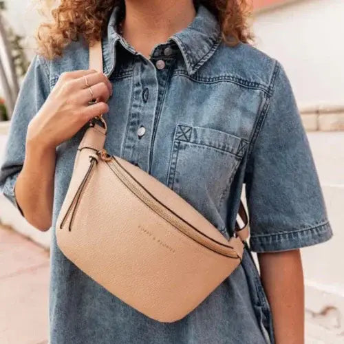 Person wearing a beige crossbody bag with a denim shirt outdoors