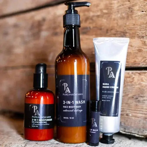 Pure Anada Men’s skincare products including 3-in-1 wash, 2-in-1 moisturizer, shea hand cream, and lip balm on rustic wood background