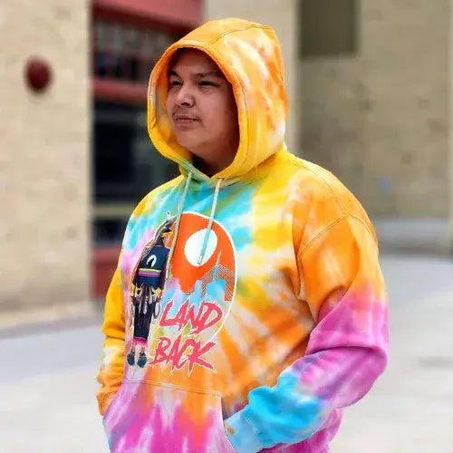 Person wearing a colorful tie-dye hoodie with graphic design outdoors.